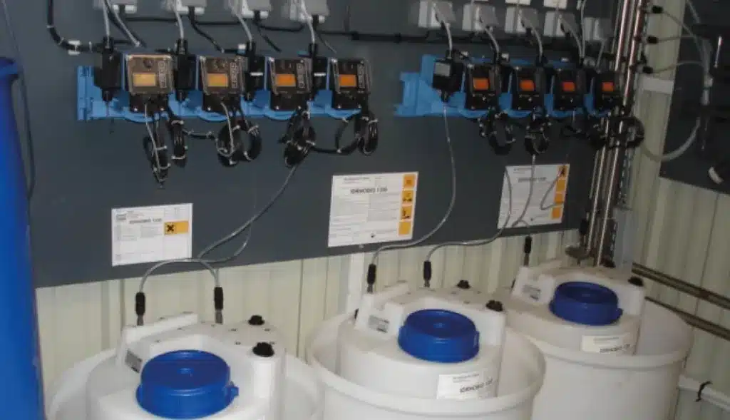Panel de bombas dosificadoras Ecolab instaladas en pared con tanques de producto químico